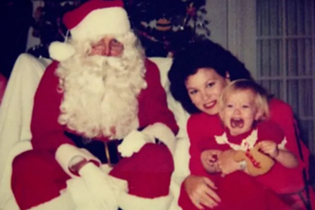 Hilary Duff de vestidinho vermelho, apavorada no colo da mãe, ao lado do Papai Noel
