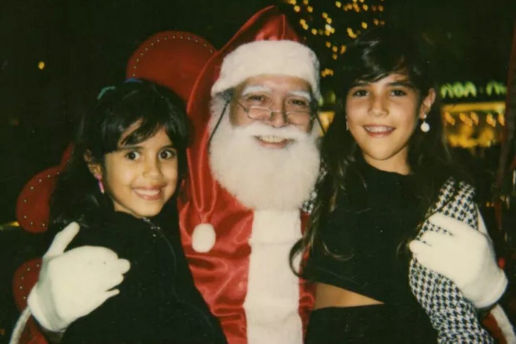 Papai Noel abraçado às irmãs Camilla Camargo  e Wanessa, ambas de preto, sorrindo