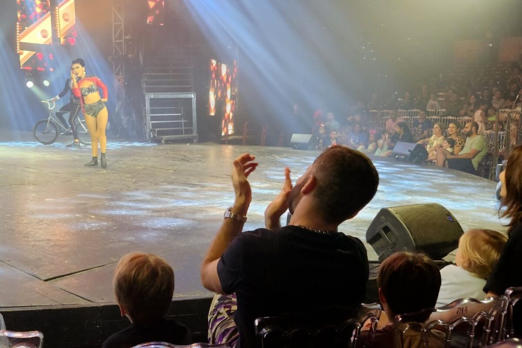Thales Bretas de camisa preta, dentro do circo com os filhos, aplaudindo a apresentação