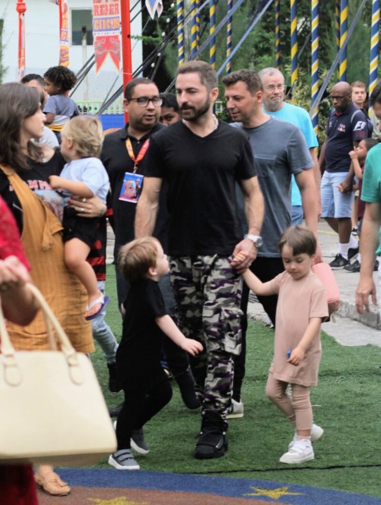 camisa preta, calça camuflada, de mãos dadas com os filhos, chegando ao circo