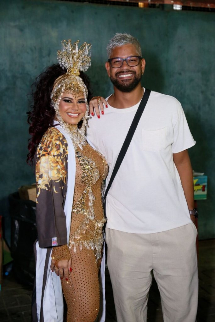 Viviane Araújo de biquíni dourado e roupão abraçada ao marido, na Cidade do Samba