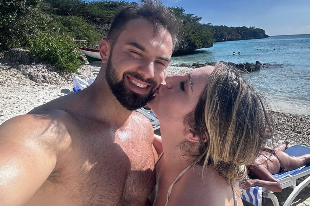 Amanda dando beijo no rosto de Felipe Weiber, em uma praia