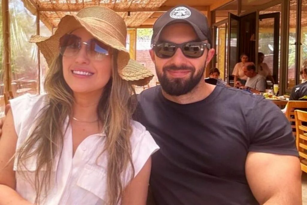 Amanda de chapéu e camisa branca, sentada ao lado de Felipe Weiber, de camisa preta e óculos escuros