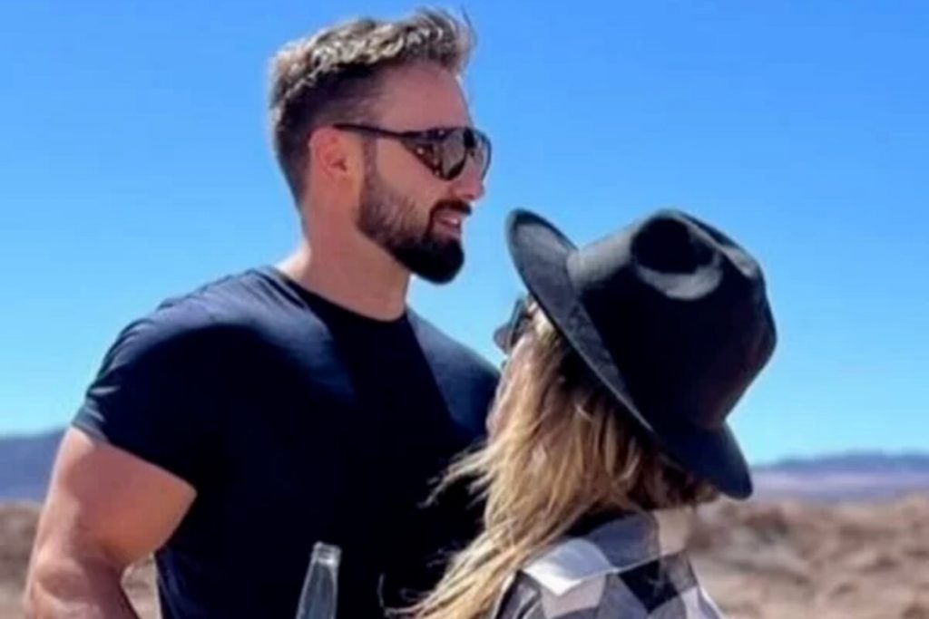 Felipe Weiber de camisa preta e óculos escuros, Amanda de chapéu preto e camisa quadriculada, se olhando