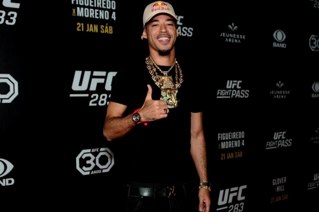 L7nnon fazendo sinal de positivo, de roupa preta e cordão de ouro