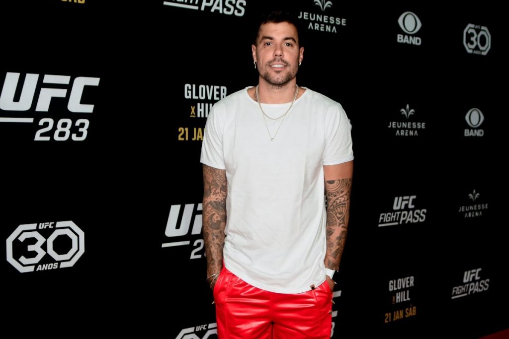 Lipe Ribeiro de camisa branca, calça vermelha, mãos no bolso