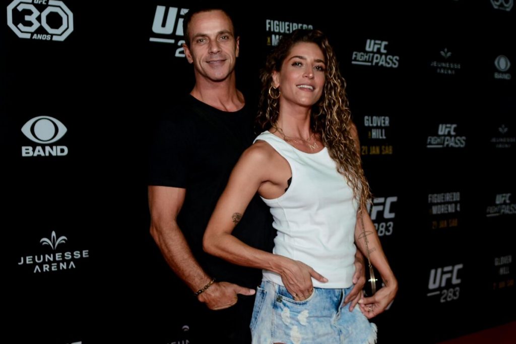 Maria Joana de camiseta branca, saia jeans, abraçada ao namorado, Bernardo Muniz