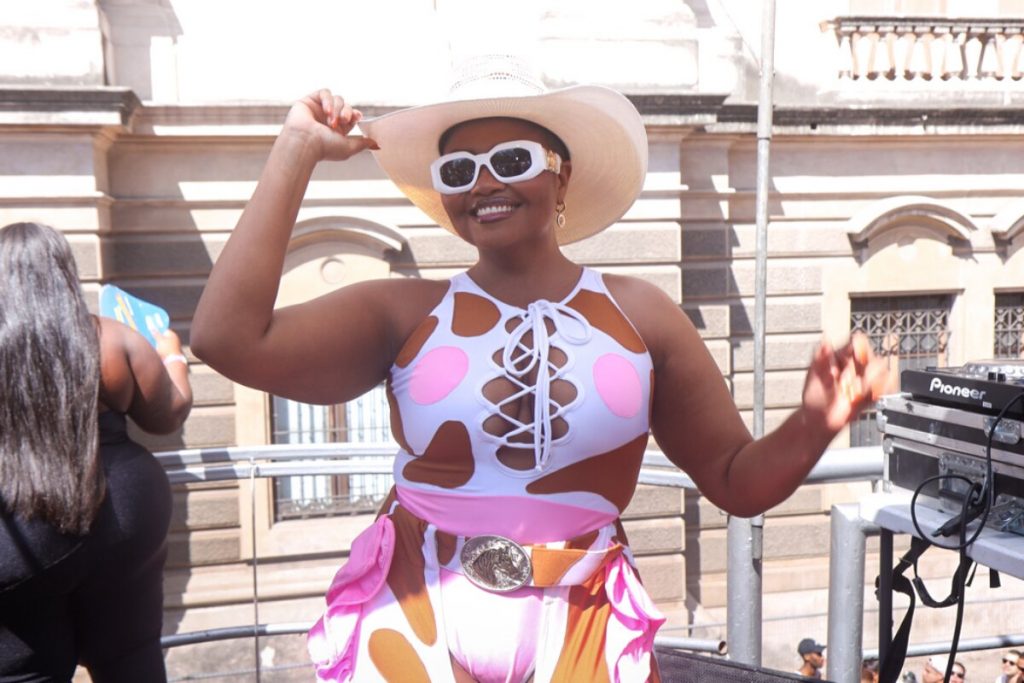 Gaby Amarantos de macacão estilizado branco e rosa, chapéu e óculos escuros