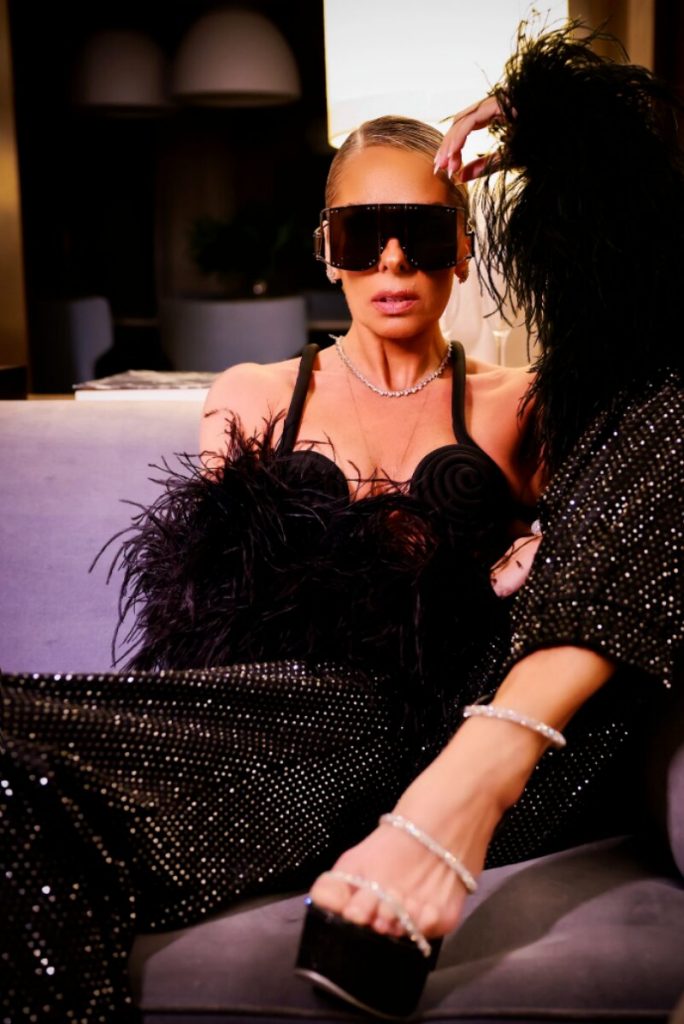 Adriane Galisteu de óculos escuros,  calça preta brilhosa e sutiã preto