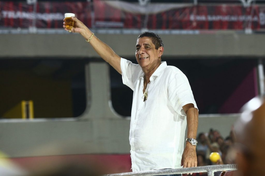 Zeca Pagodinho de camisa branca segurando copo de cerveja, no ensaio técnico da Grande Rio na Sapucaí 