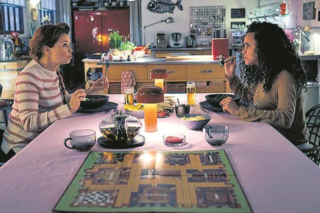Cena do filme de Domitila Barros, ela sentada à mesa com outra atriz 