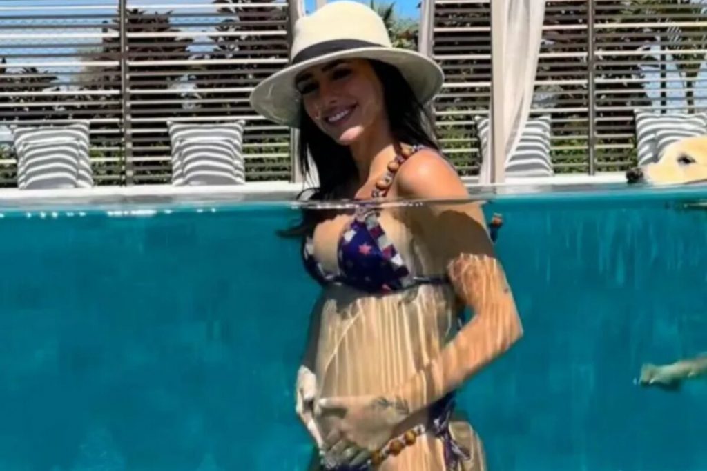 Bruna Biancardi na piscina, de biquíni e chapéu, com as mãos na barriga 