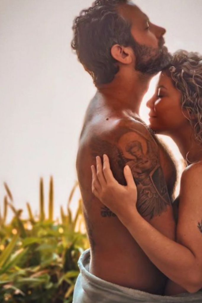 Bárbara Borges e iran Malfitano em momento carinhoso, em porta de varanda, nus