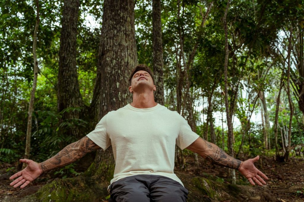 Fernando Fernandes de braços abertos, olhando para o alto, na Amazônia, gravando o No Limite