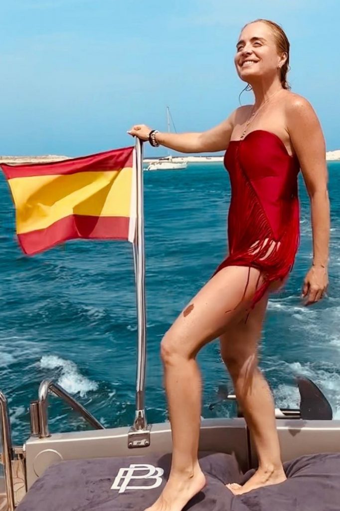 Angélica de maiô vermelho apoiada no mastro da bandeira da Espanha 