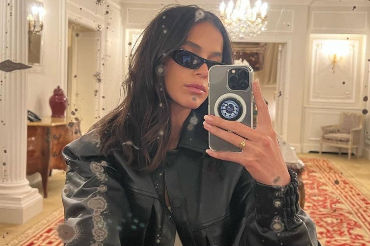 bruna marquezine tirando selfie com casaco preto e óculos escuros