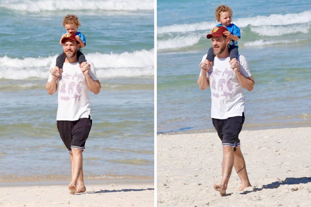 Emílio Dantas caminha com filho no ombro pela praia
