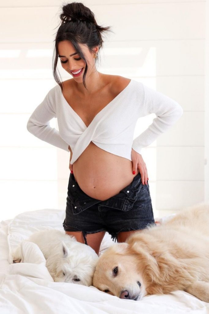 Bruna Biancardi de cropped branco   short preto, ajoelhada com a mão na barriga, com seus dois pets, um branco e outro caramelo
