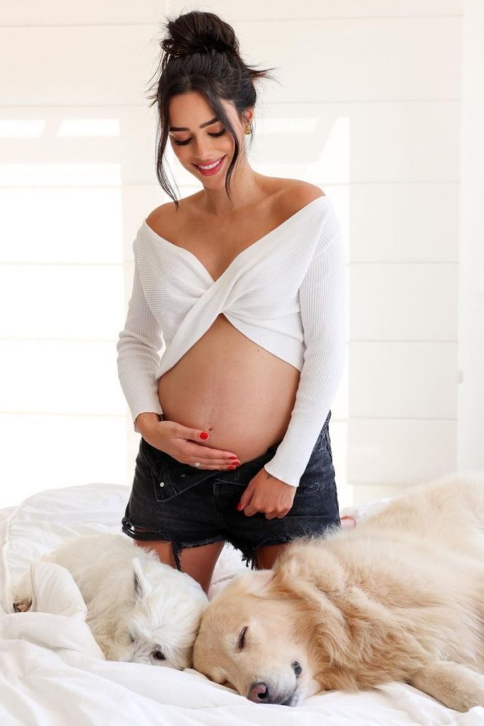 Bruna Biancardi de cropped branco   short preto, ajoelhada com a mão na barriga, com seus dois pets, um branco e outro caramelo