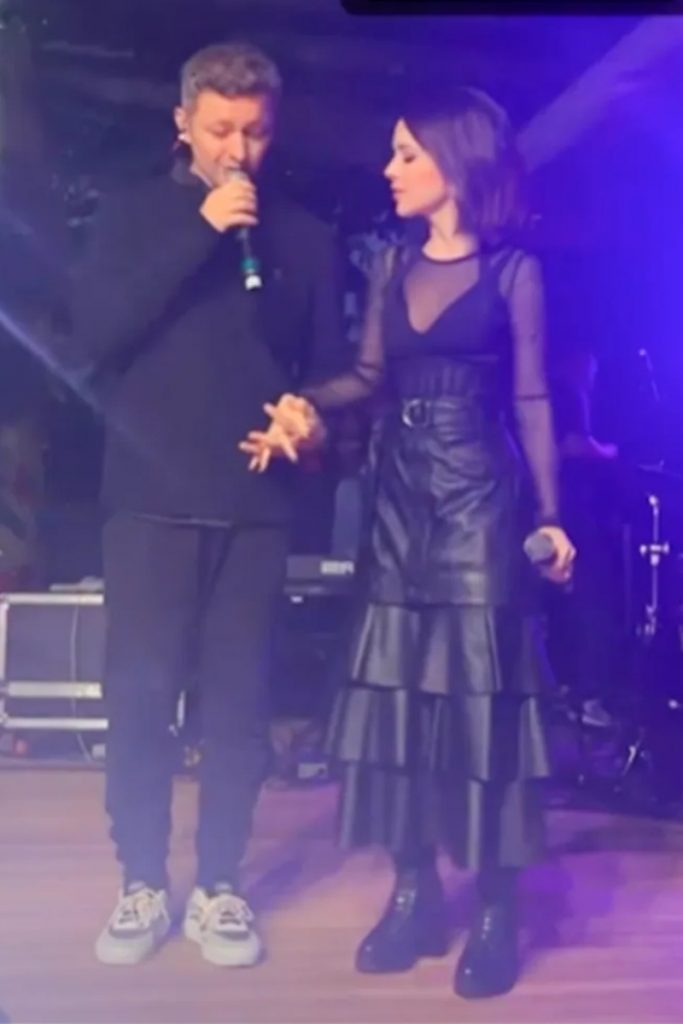 Lucas Lima de preto, de mãos dadas com Sandy de vestido preto, cambos no palco