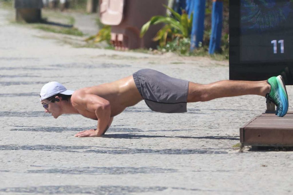 Nicolas Prattes sem camisa se exercitando na orla da praia