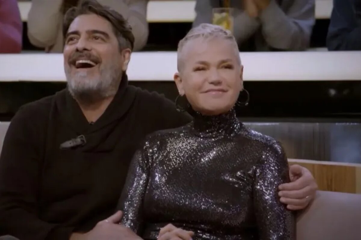 Junno Andrade e Xuxa Meneghel sentados, sorrindo, no programa 'Sobre Nós Dois"