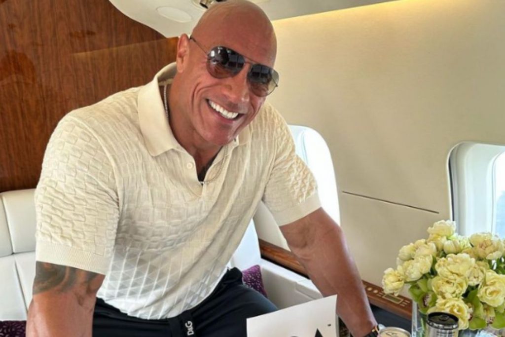 Dwayne Johnson, o The Rock, posa  sorrindo e com óculos escuros