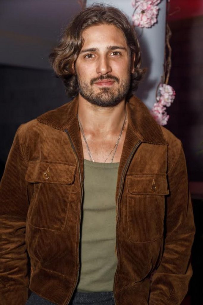Daniel Rocha posa de casaco marrom, em festa de Cleo