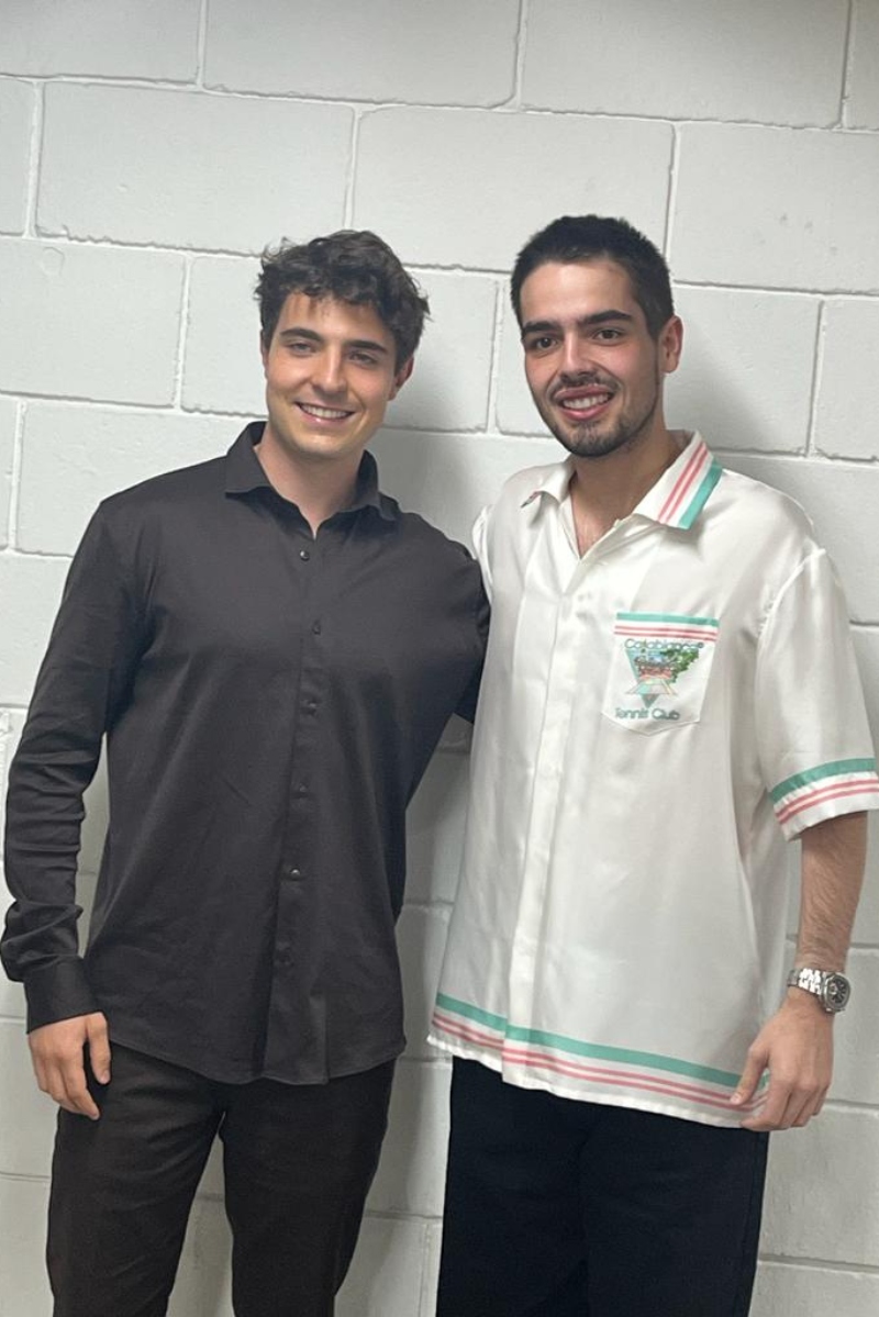 João Augusto Liberato de camisa social marrom, ao lado de João Guilherme Silva, de camisa branca, ambos sorrindo 