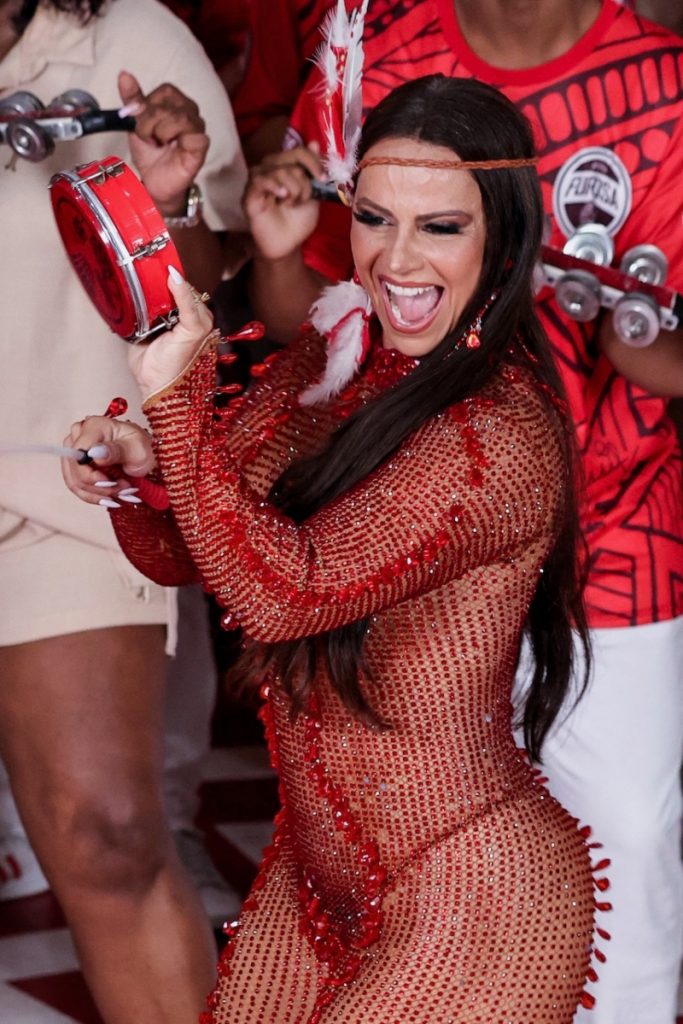 Viviane Araújo de macacão de meia arrastão vazado vermelho, biquíni vermelho tocando tamborim