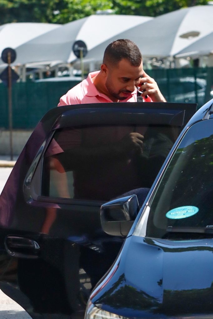 Gil do Vigor de camisa polo rosa e bermuda nude, falando ao telefone, entrando no carro