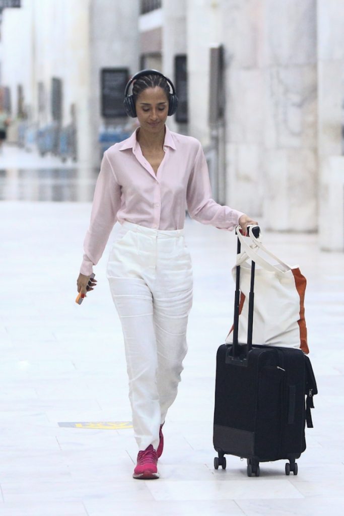 Camila Pitanga de calça branca, camisa social de manga cor de rosa fone de ouvido, com mala, desembarcando no aeroporto 