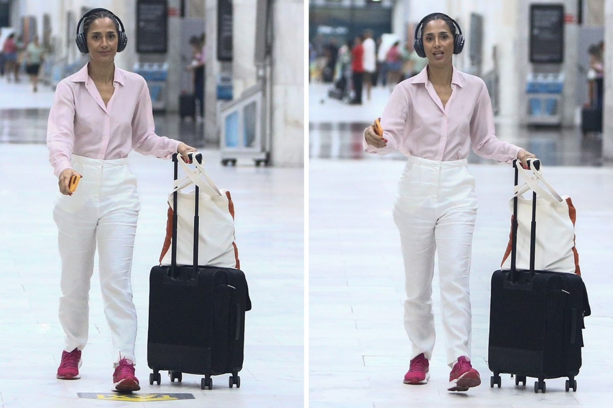 Camila Pitanga de calça branca, camisa social de manga cor de rosa fone de ouvido, com mala, desembarcando no aeroporto