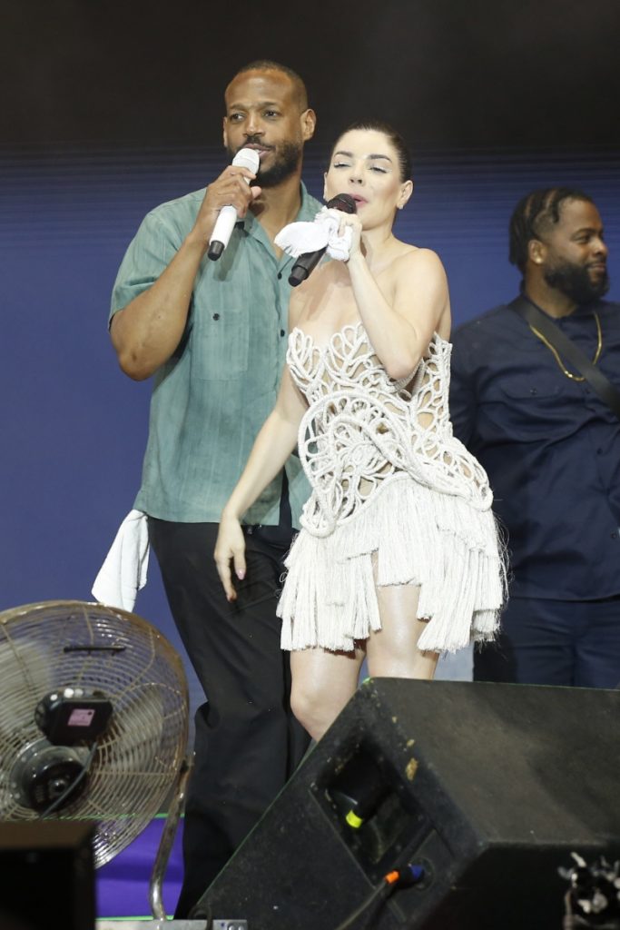 Marlon Wayans de camisa verde e calça jeans, no palco com Gkay, de vestido curto branco