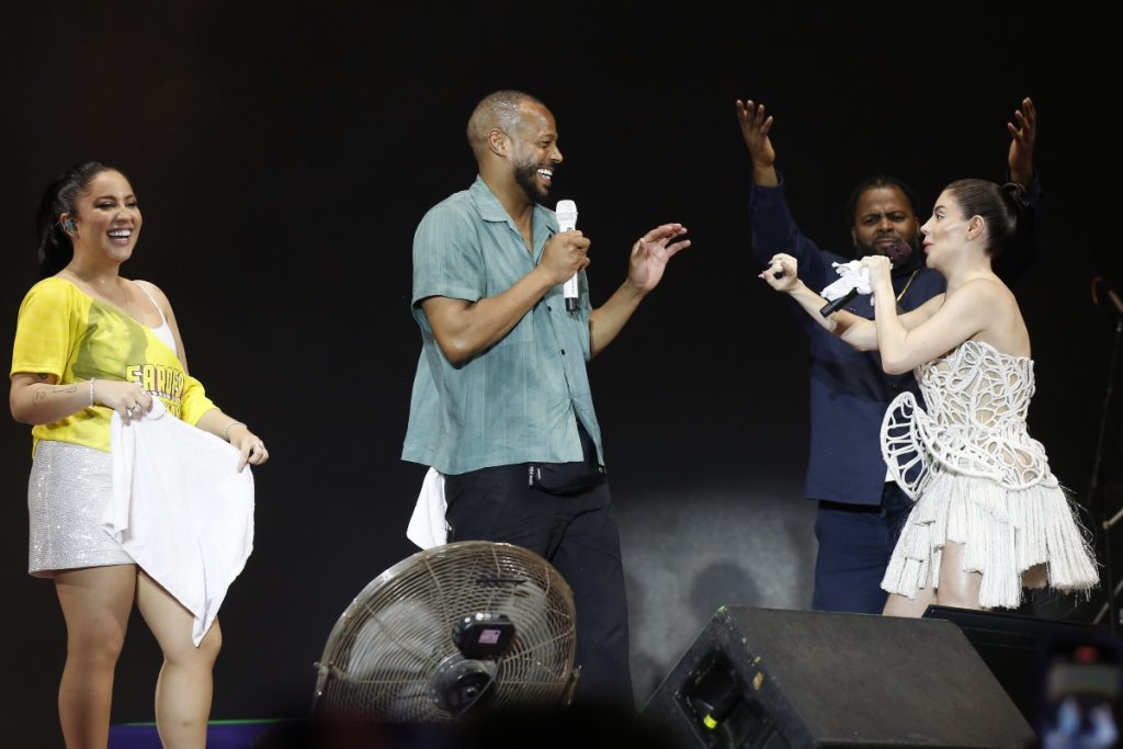 Marlon Wayans de camisa verde e calça jeans, no palco com Gkay, de vestido curto branco e Mari Fernandez de short branco e camisa amarela