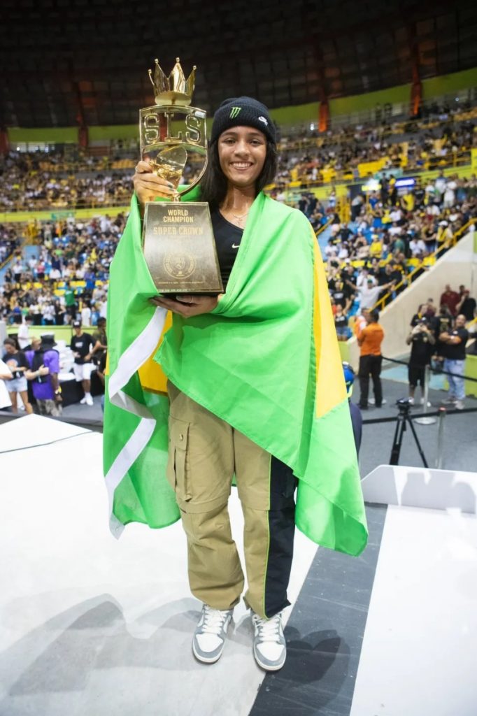 Rayssa Leal envolta na bandeira do Brasil, exibindo troféu