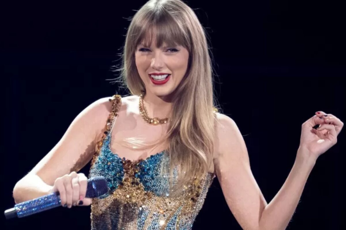Taylor Swift de vestido azul brilhante, segurando microfone, sorrindo