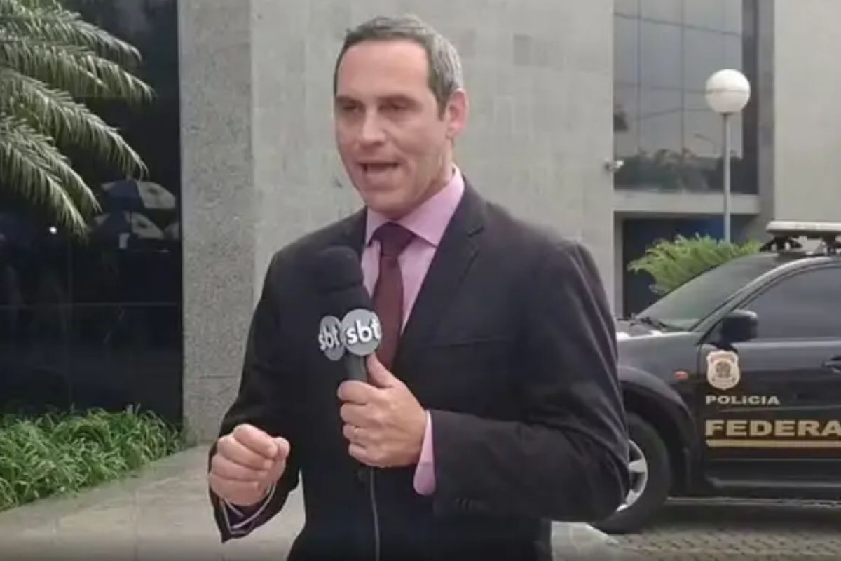 Jornalista Marcelo Carrião de terno, segurando microfone do SBT