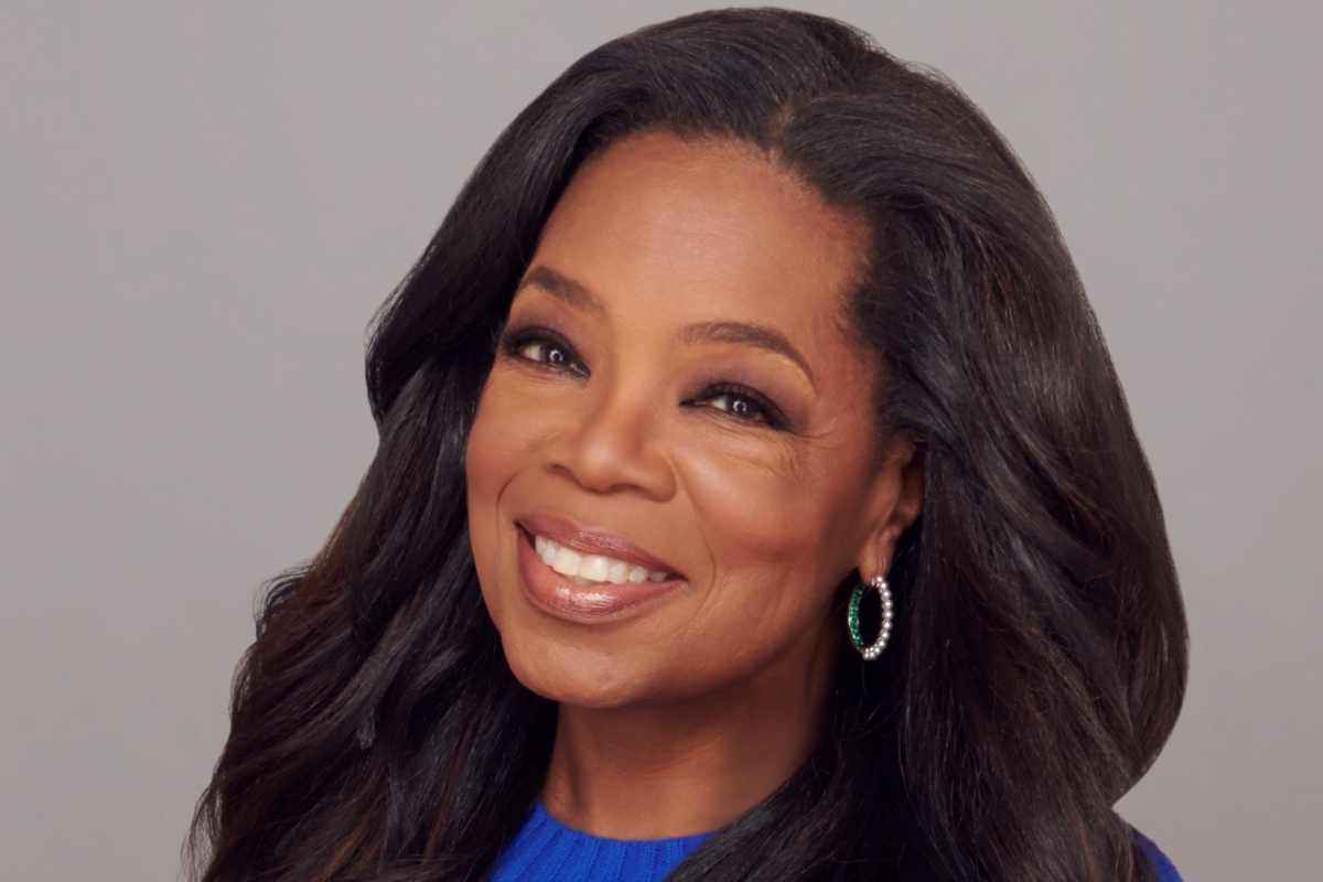 Oprah Winfrey de cabelos solos e vestido azul, sorrindo